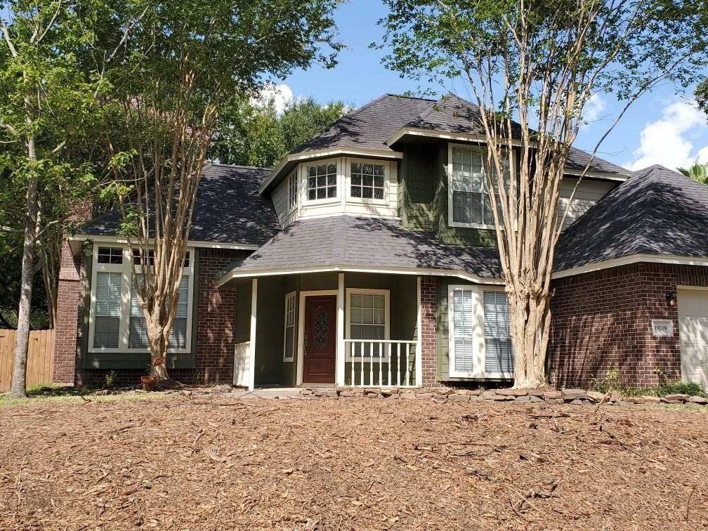 Two-story brick house with dark roof and front porch, surrounded by trees and a bare yard