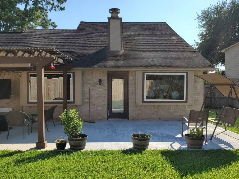 Backyard patio with a small house, covered patio, potted plants, and a lawn in sunlight