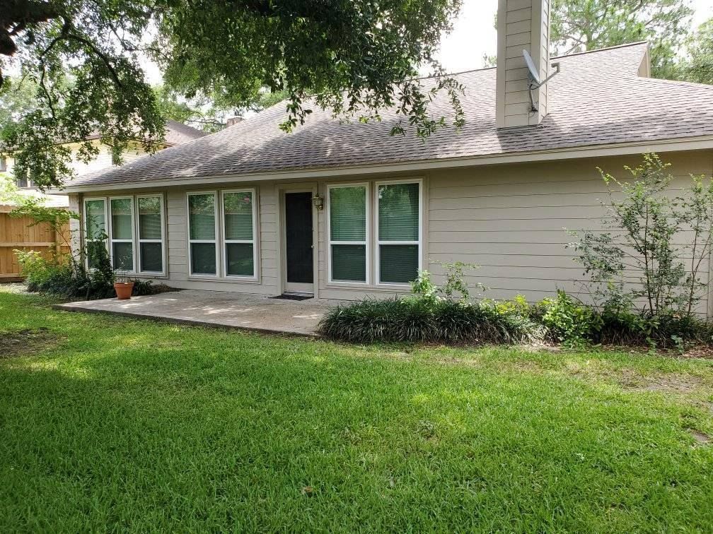 Single-story beige house with a front lawn, windows, and a small porch under trees