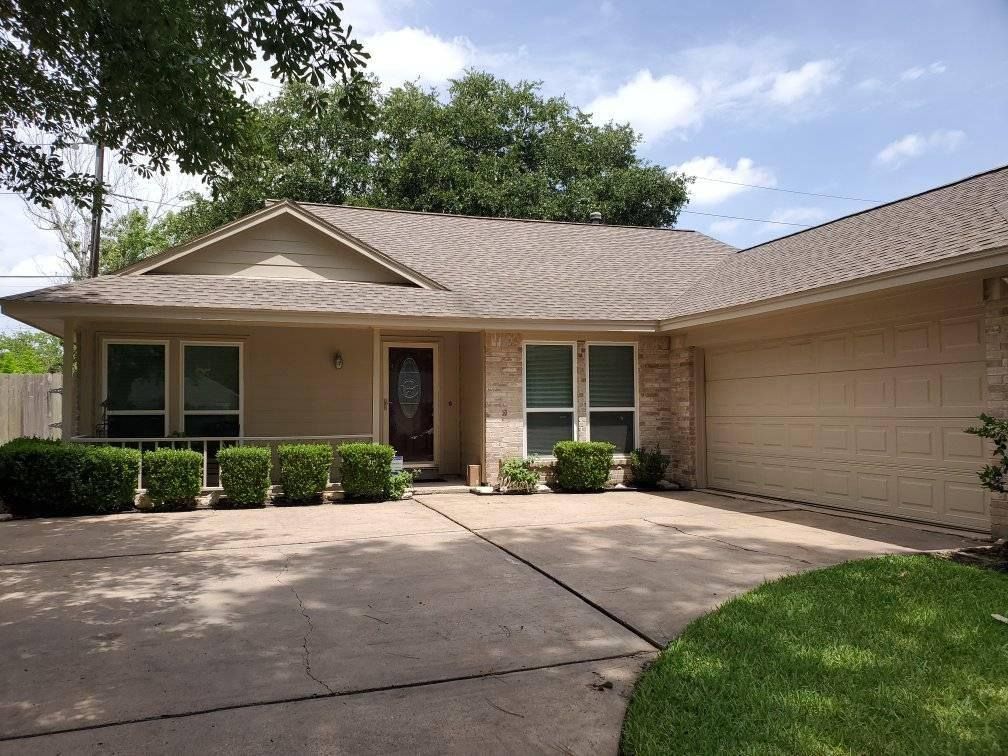 Single-story beige house with a two-car garage, front porch, and driveway under a bright sky