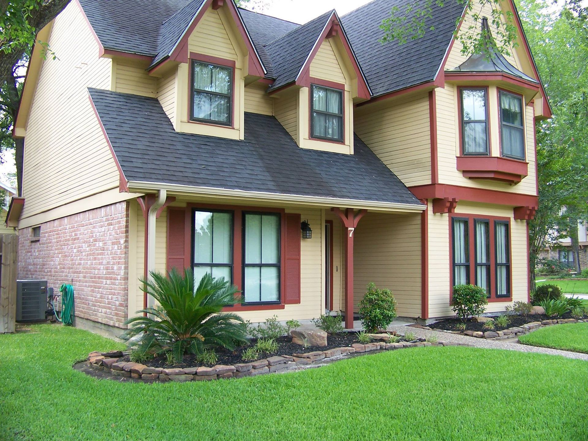 Two-story cream and red house with dark roof, front porch, bay windows, and a green lawn
