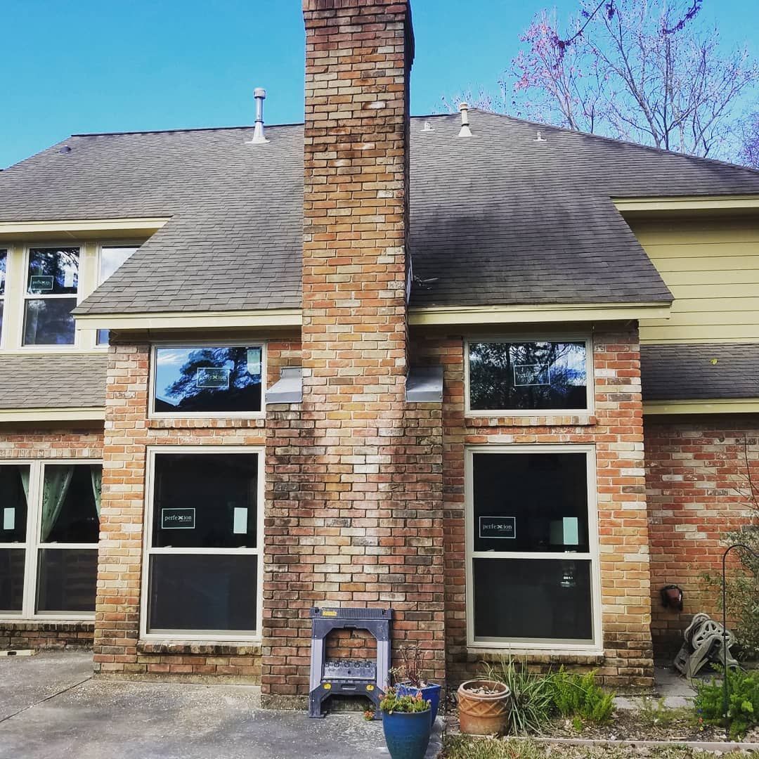 Brick house exterior with a central chimney, two front windows, and a small potted plant by the steps