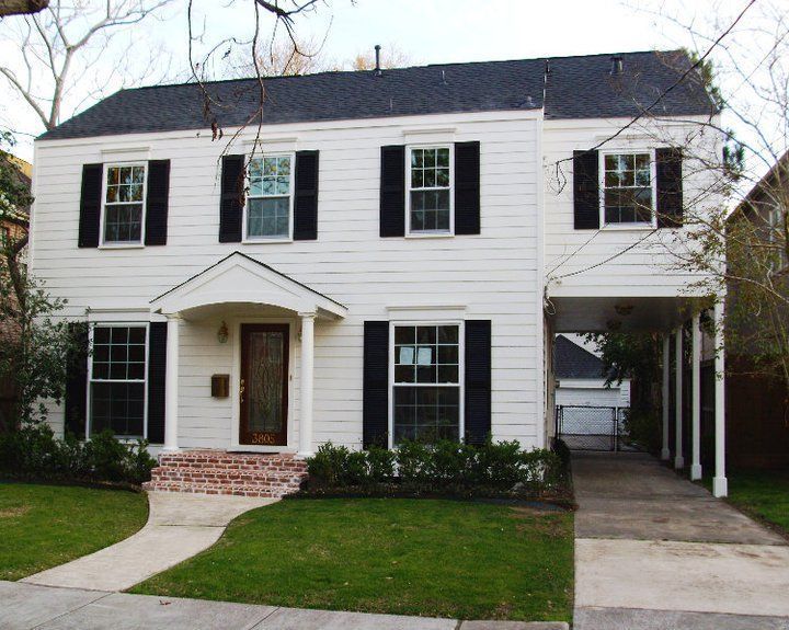 White two-story house with black shutters, a front porch, brick walkway, and driveway