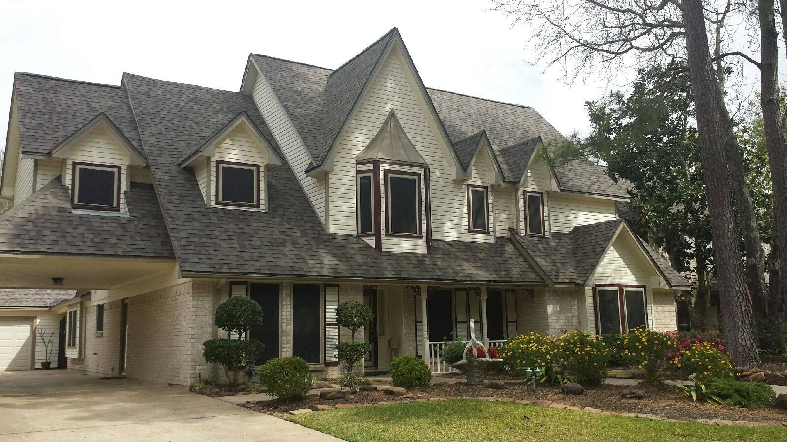 Large gray stone house with steep gabled roof, covered driveway, and landscaped front yard
