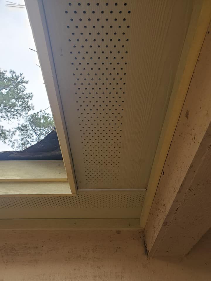 Close-up of a beige soffit and roof eaves with perforated vent panels beside a skylight.