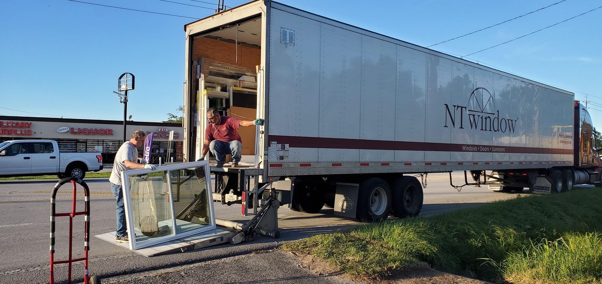 Workers unload items from a white moving truck at a roadside lot.