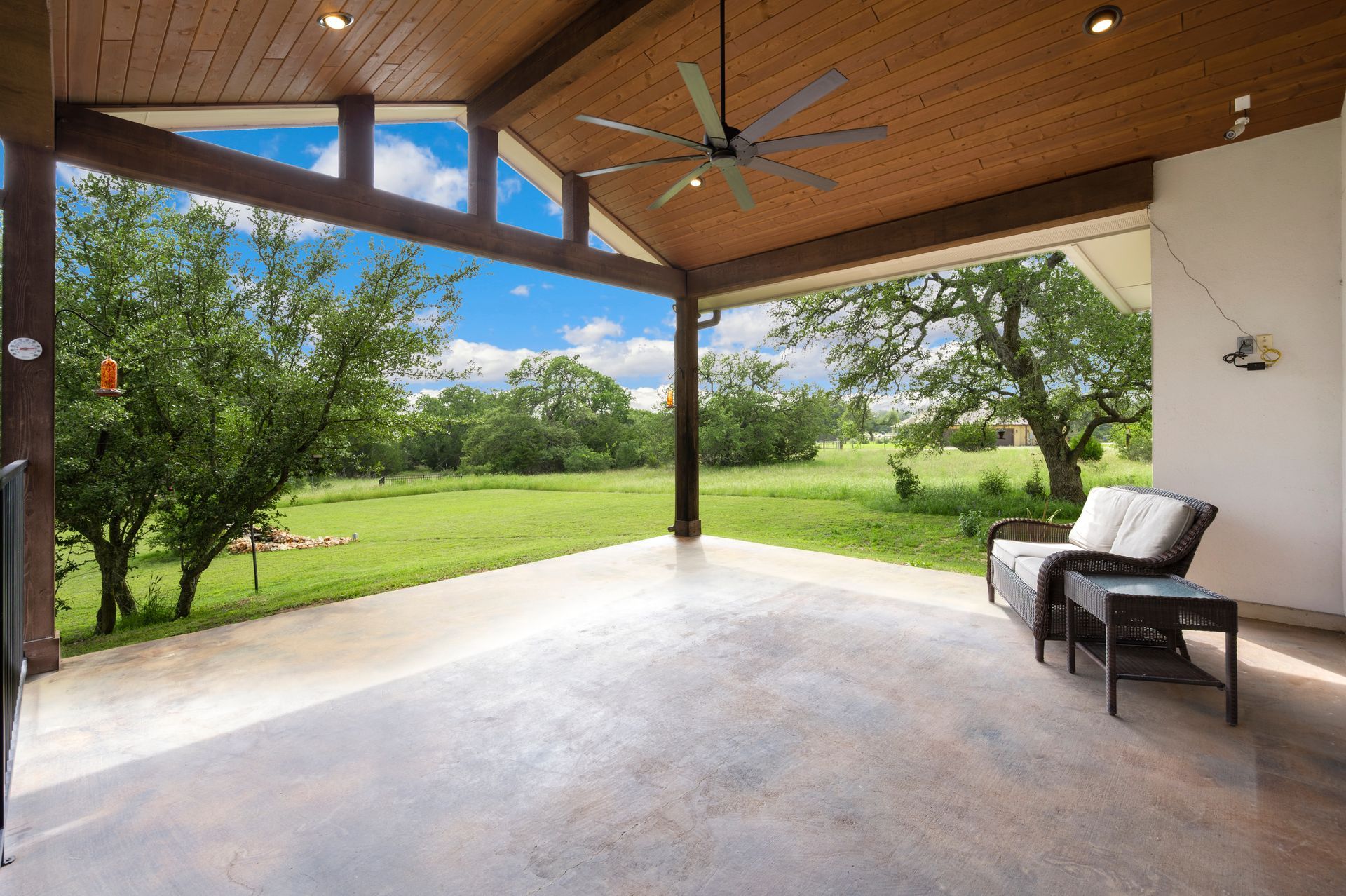 Covered patio with wood ceiling, concrete floor, and a green lawn view, with a lounge chair on the right
