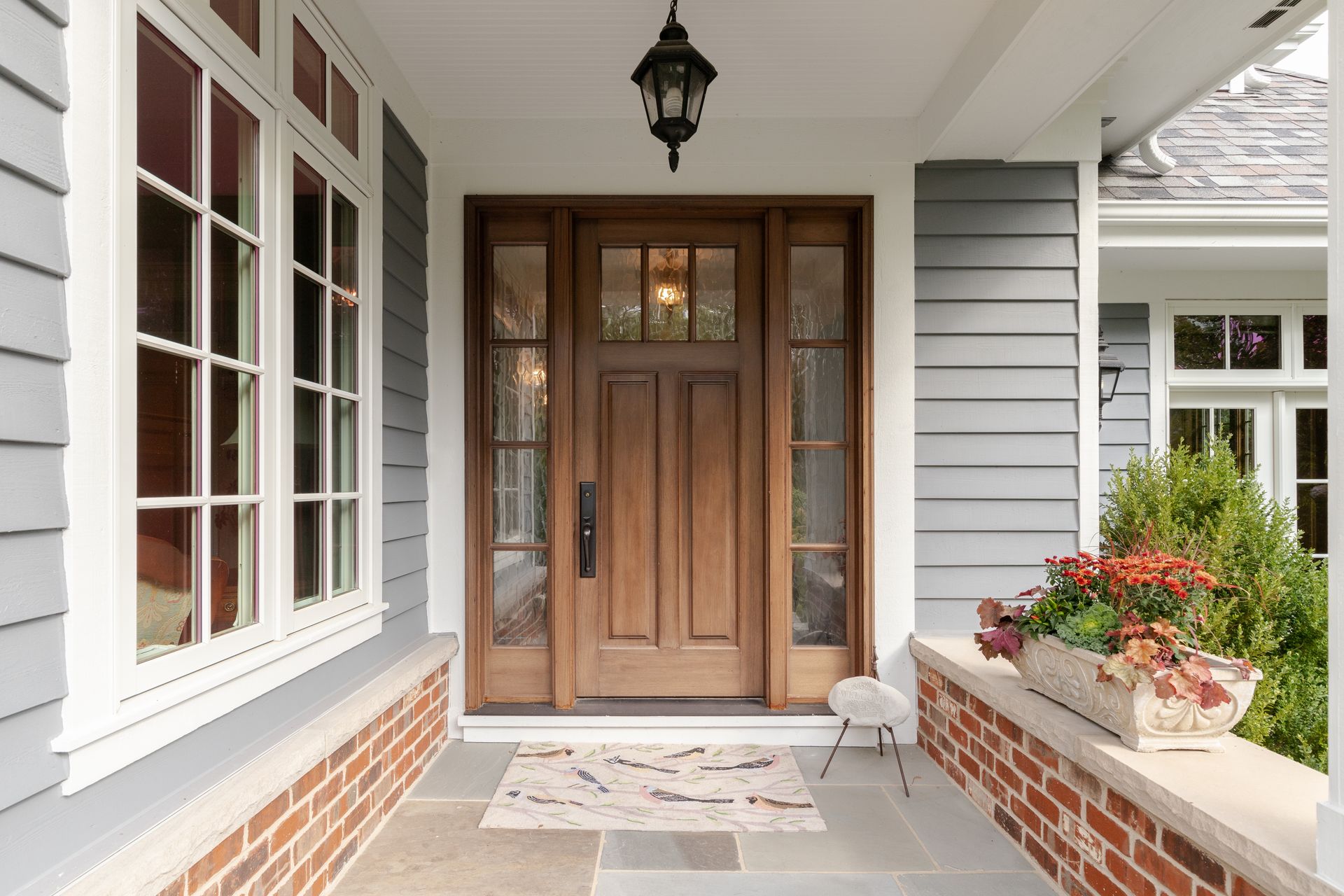 Front porch with wooden double doors, brick planters, and gray siding.