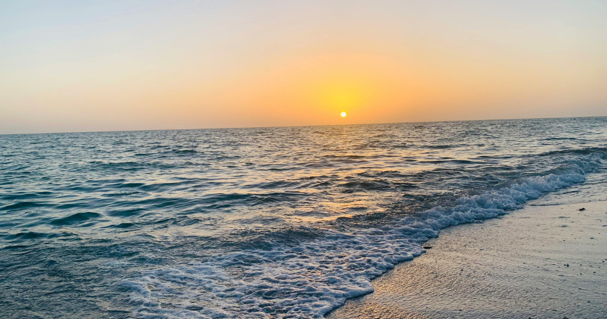 Sunset over a choppy ocean with waves washing onto a sandy shore
