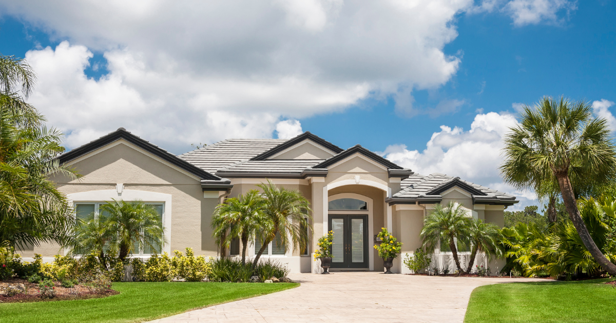 Modern single-story suburban home with a landscaped lawn, palm trees, and a bright blue sky.