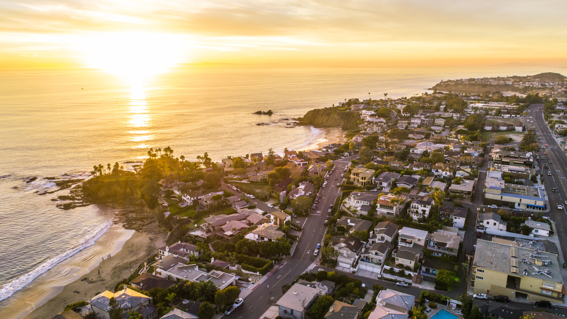 Sunset over a coastal neighborhood beside the ocean, with golden light reflecting on the water