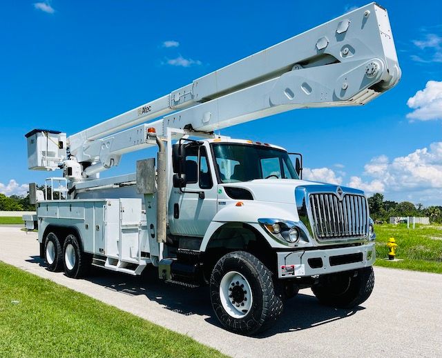 A white truck with a crane on top of it is parked on the side of the road.