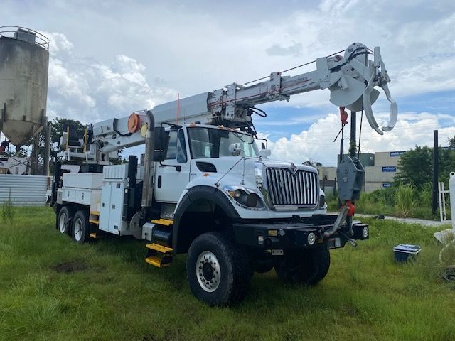 White utility truck with a boom lift parked on grass near industrial buildings.