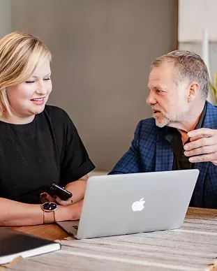 A man and a woman are sitting at a table looking at a laptop.