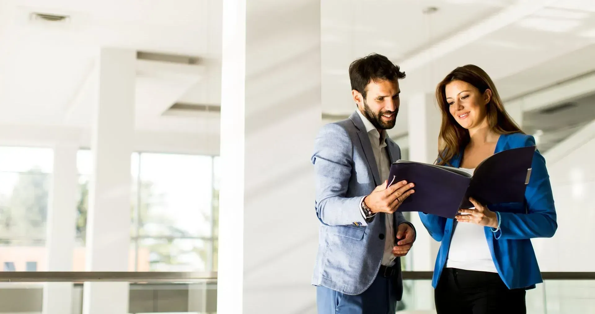 A man and a woman are looking at a clipboard in an office.