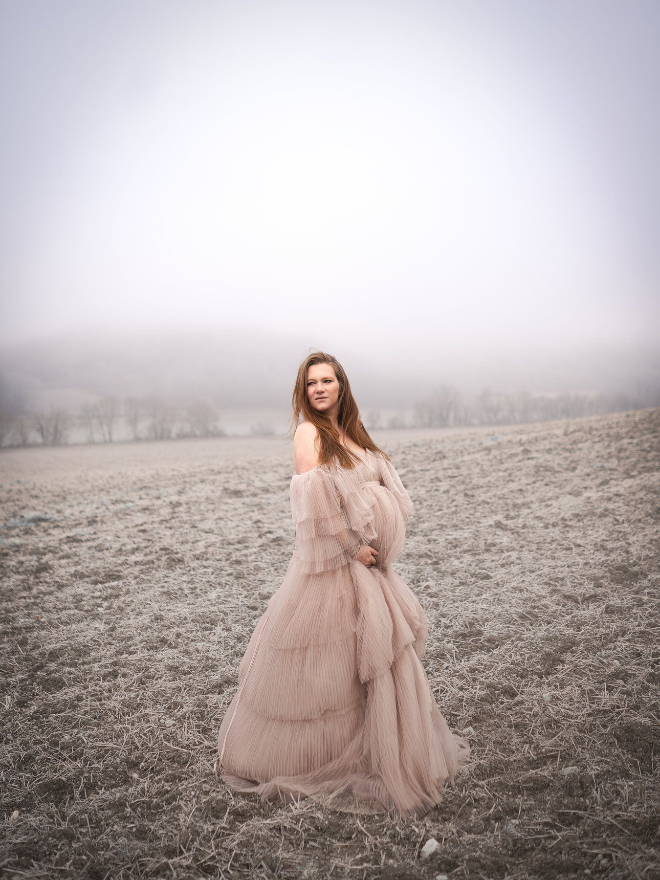 Une femme enceinte dans une longue robe se tient debout dans un champ.