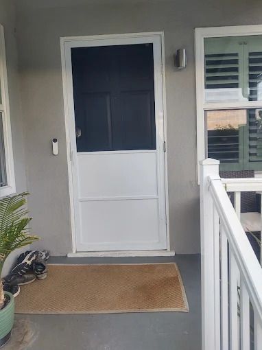 Front porch with a white screen door, tan mat, gray walls, potted plant, and white railing.