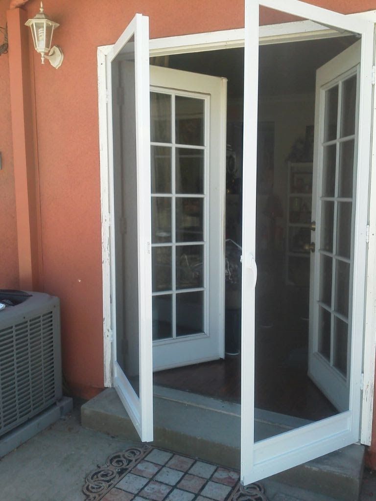 Open white French doors leading to a patio, beside a wall-mounted outdoor air conditioner.