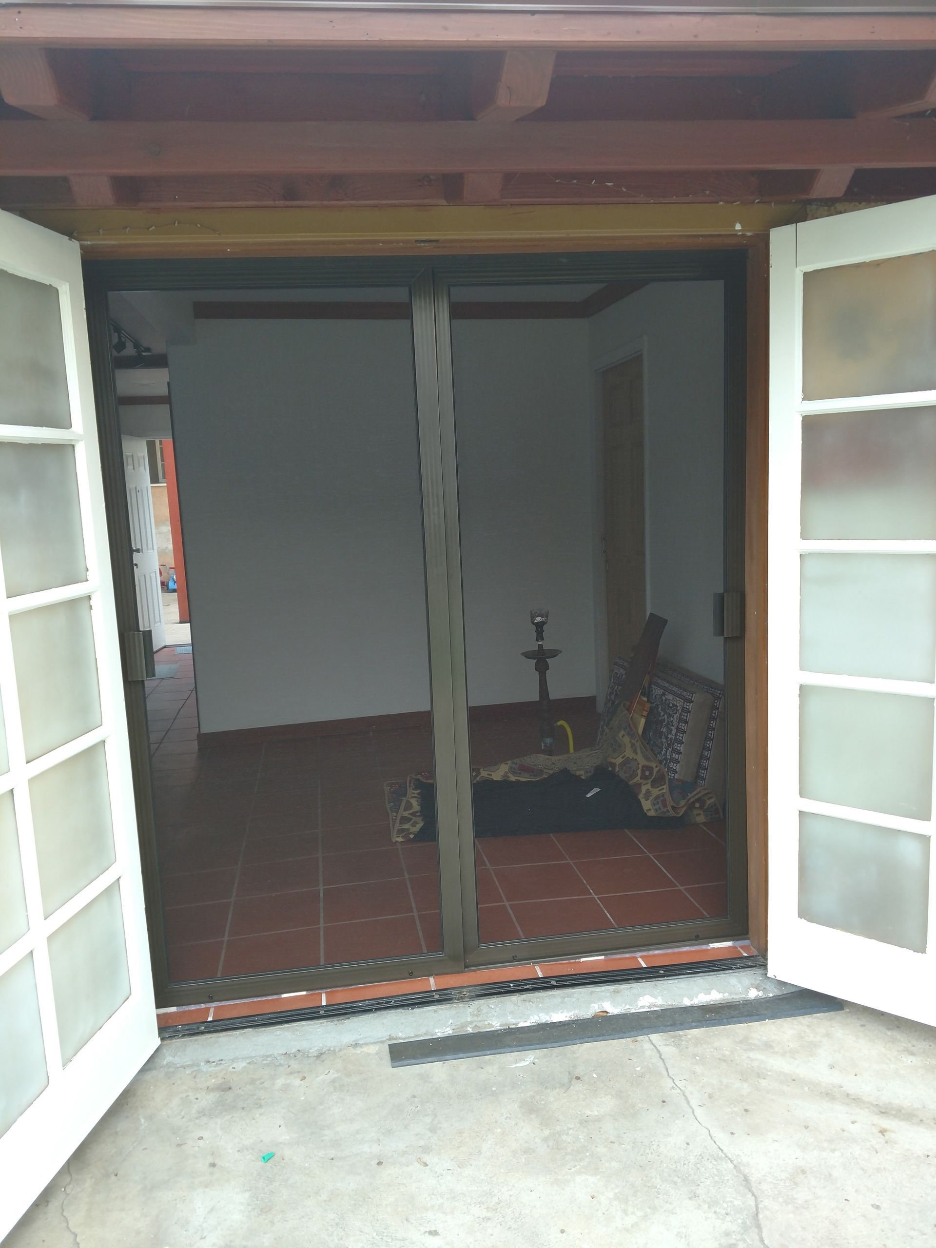 Open double doors to a tiled interior room with a chair and narrow table, viewed from outside.