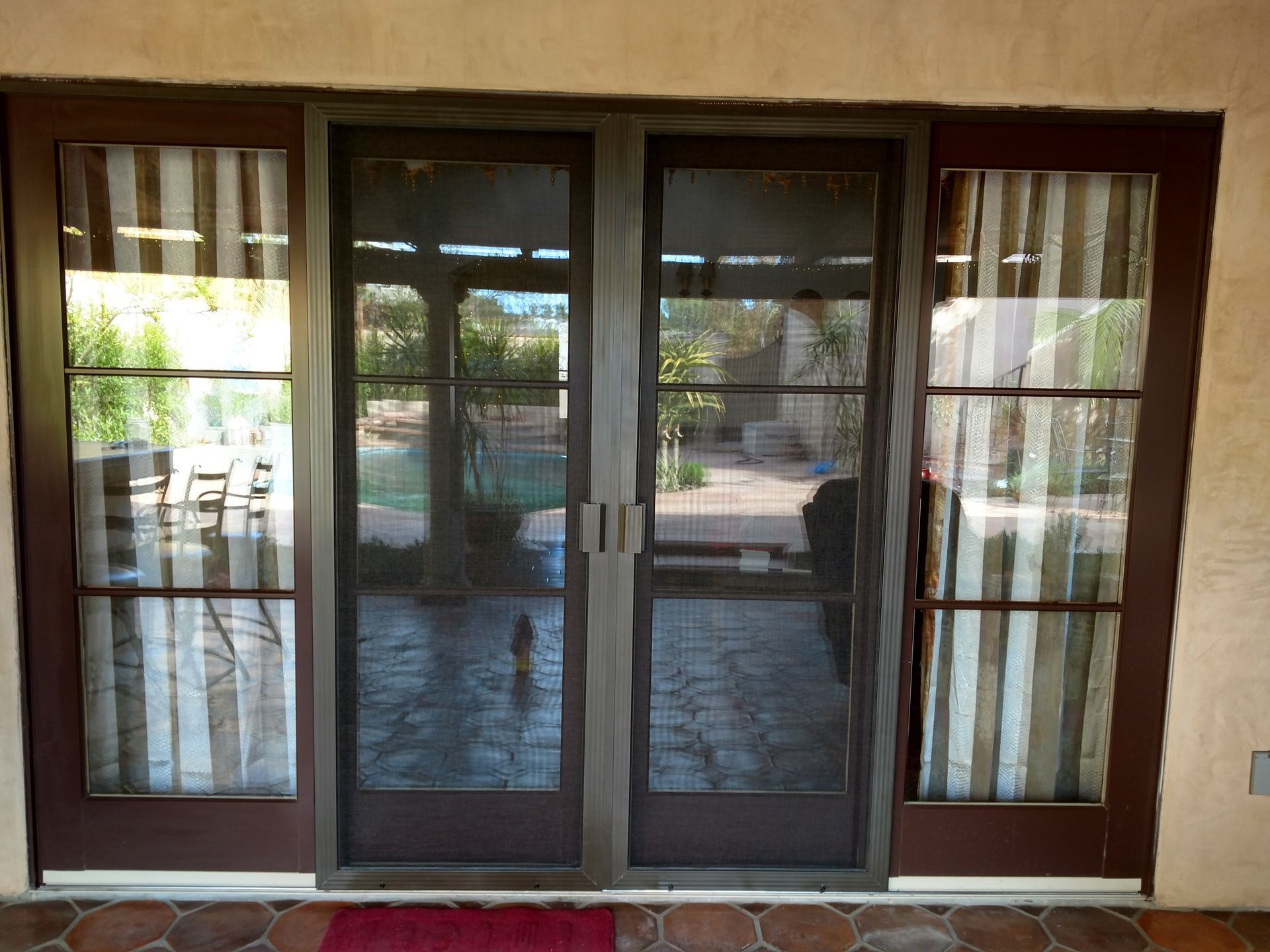 Dark-framed sliding glass doors with curtains, reflecting an outdoor patio and greenery