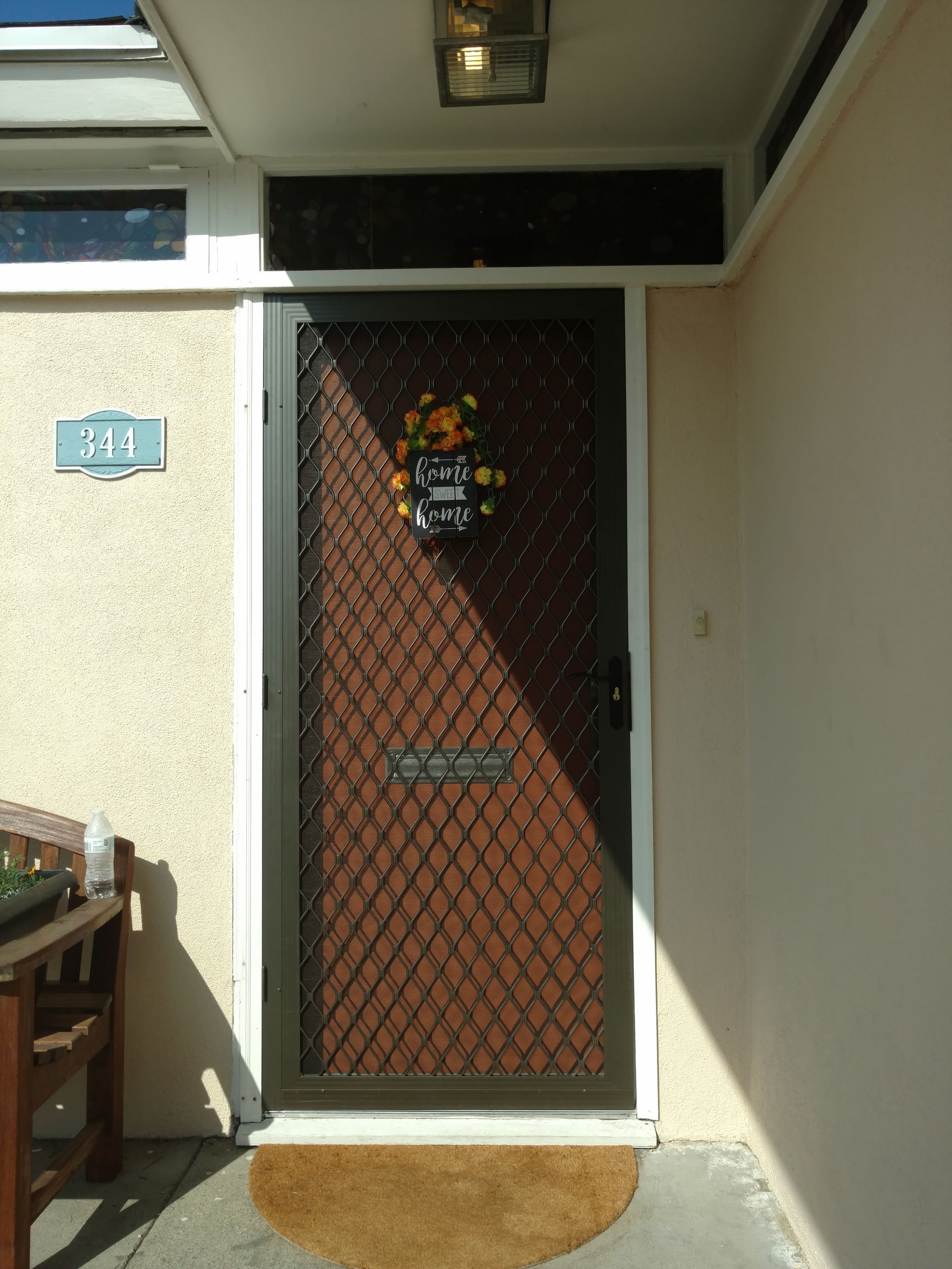 Front door with brown mesh security screen in a narrow beige entryway.