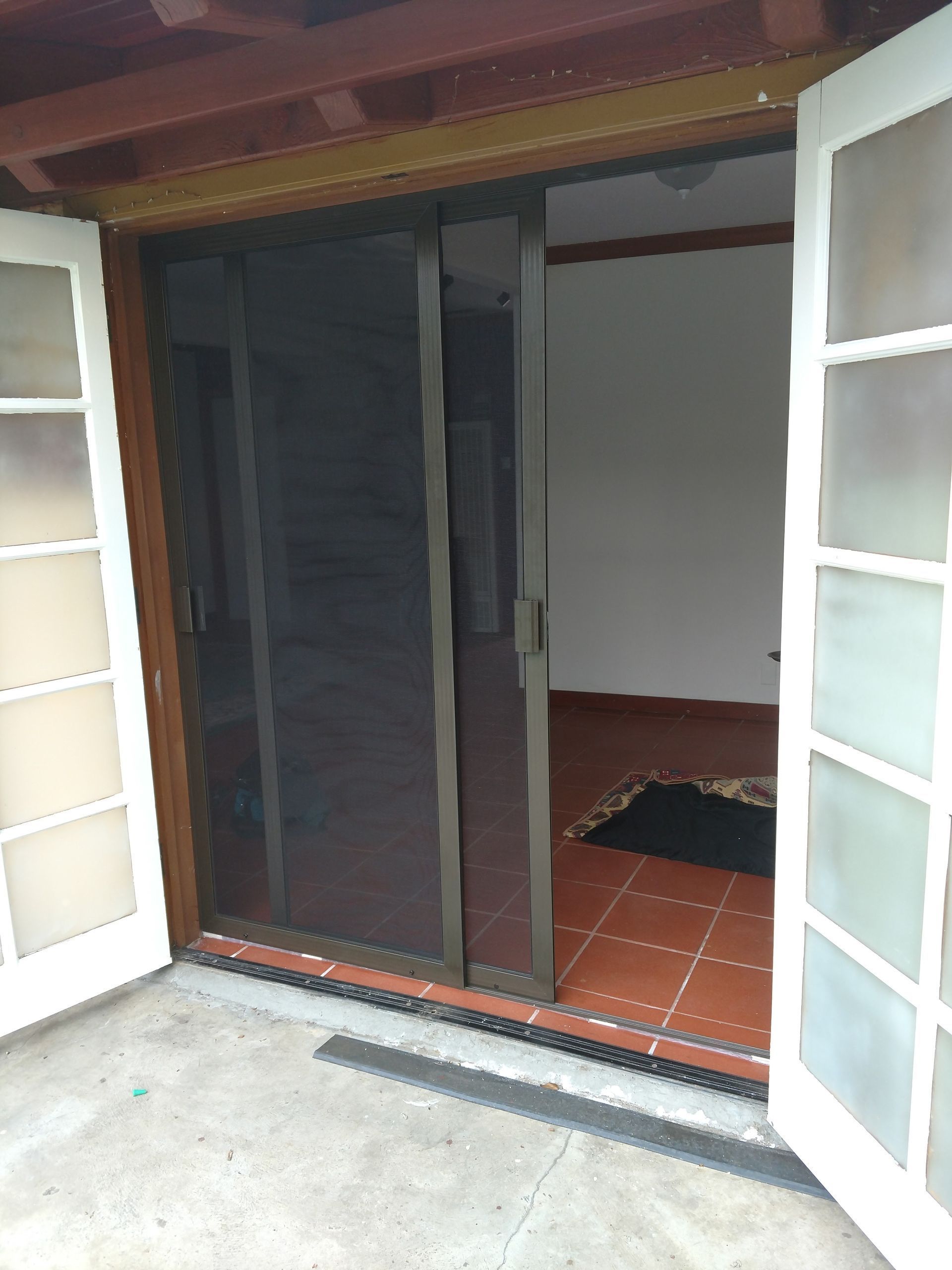 Open white French doors leading to a dim interior room with red tile floor and a doormat.