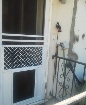White metal security door beside a wall-mounted faucet and small iron railing on a porch