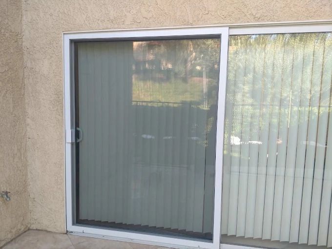 Sliding glass patio door with vertical blinds, partly closed against a stucco wall