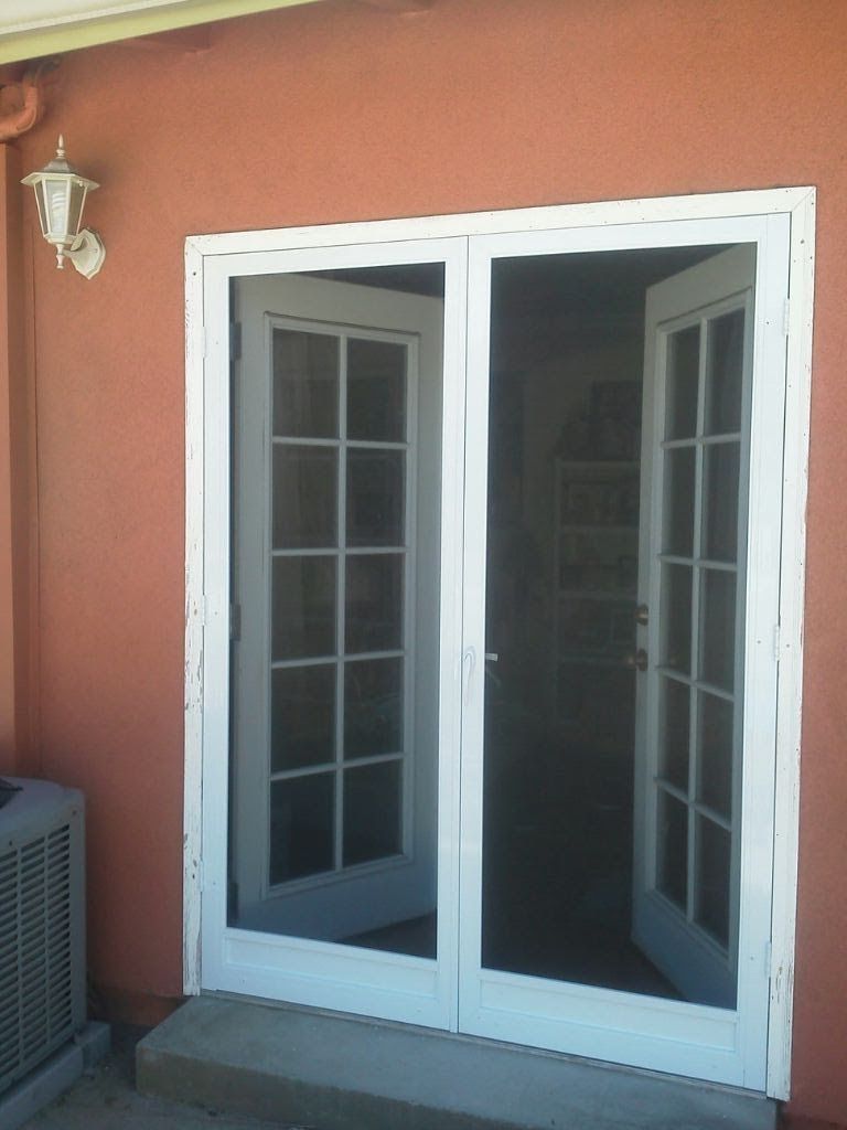 White-framed open French doors on a terracotta wall beside a small outdoor light.