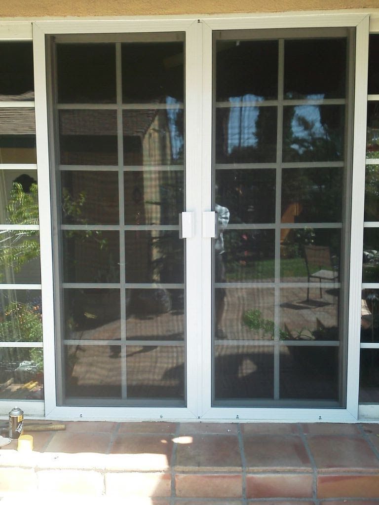 White-framed glass sliding patio doors reflecting a backyard and outdoor furniture.