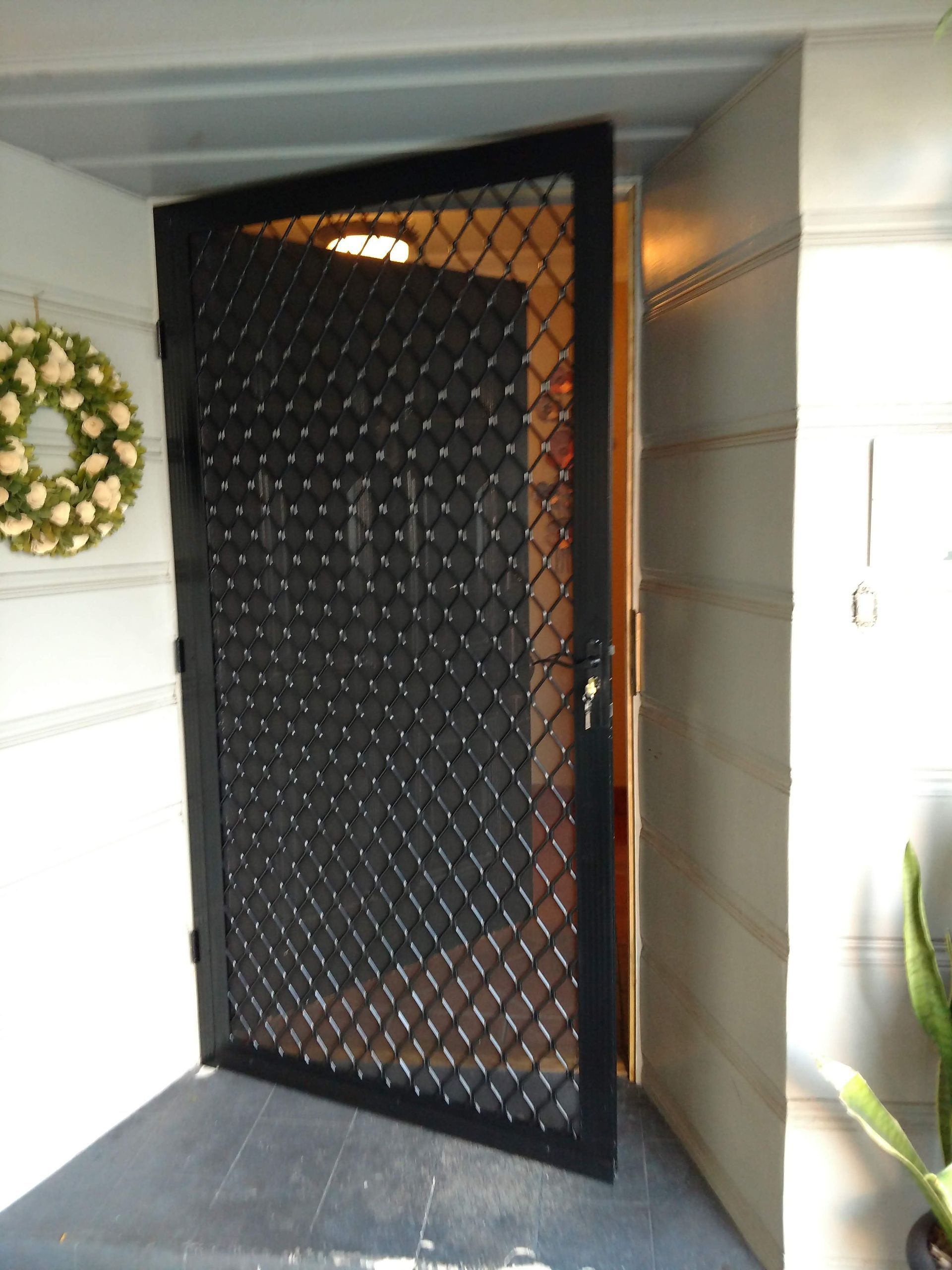 Black security screen door in a white entryway with a wreath on the wall