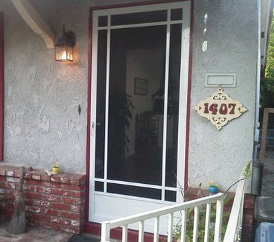 Front porch with a screen door, wall lantern, and a house number plaque reading 1907