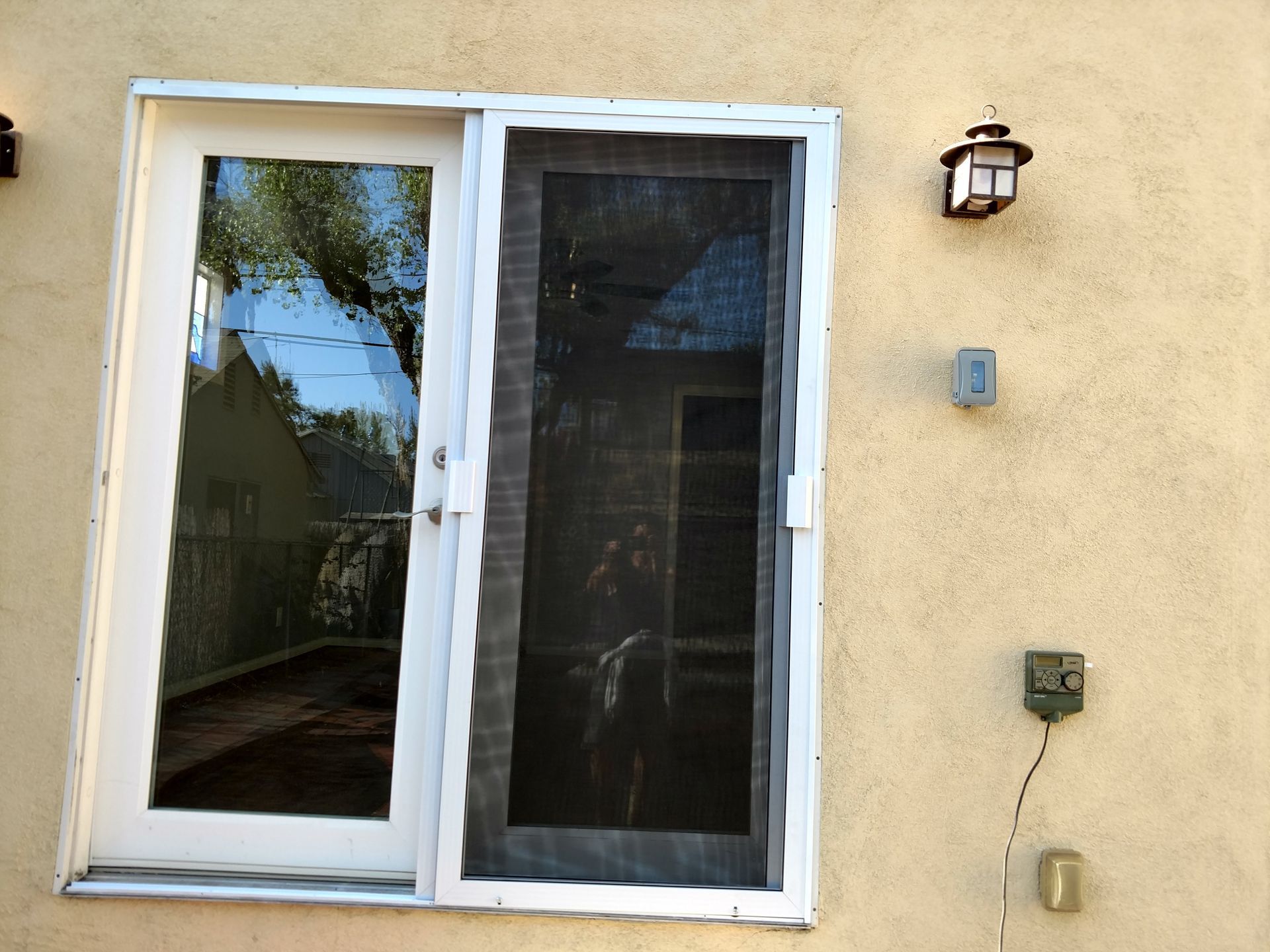 Sliding glass patio door on a beige stucco wall with an outdoor light and utility boxes nearby