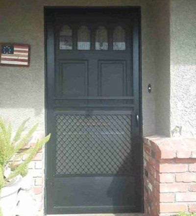 Black security screen door at a house entrance with brick wall and American flag plaque.