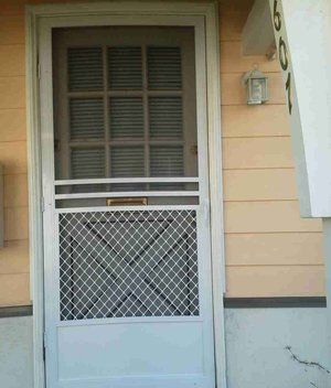 Front door with white screen door, diamond-pattern mesh, and peach siding on a house