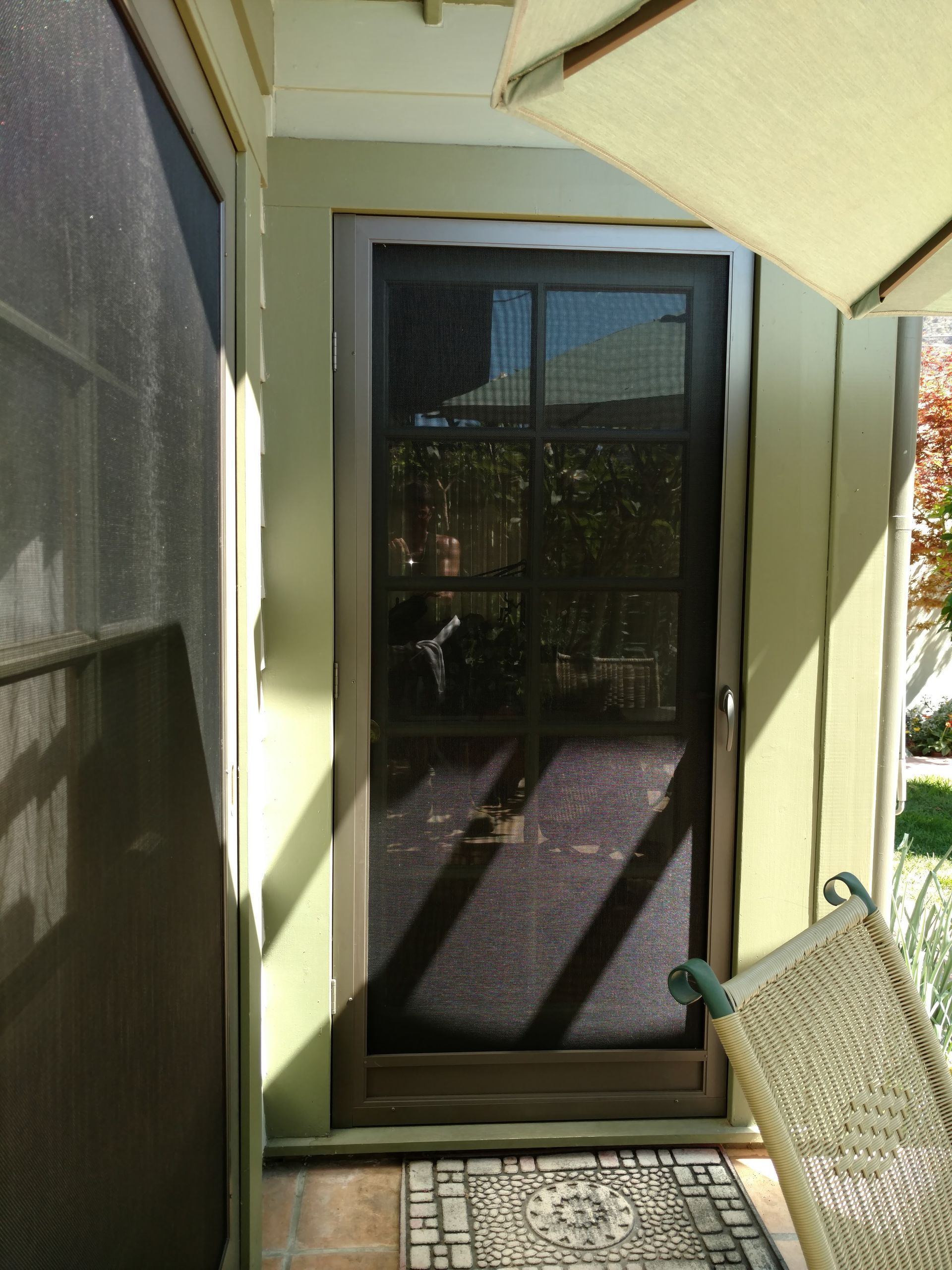Screened patio doorway with a dark glass door, pale green walls, and wicker chair in sunlight