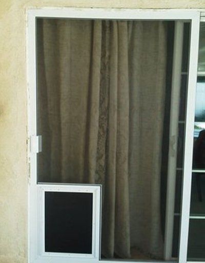 White-framed screen door with beige curtains behind it and a small pet door at the bottom left