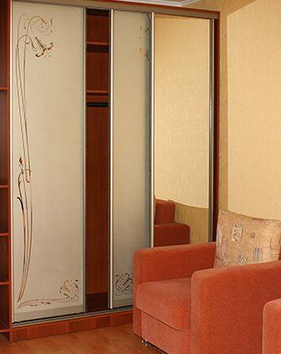 Mirrored wardrobe in a beige room beside an orange armchair and patterned cushion