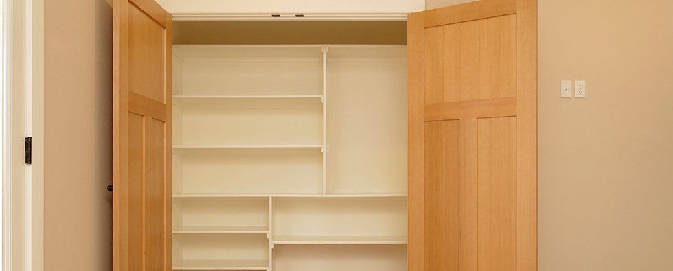 Open closet with white shelves and wooden doors in a beige room