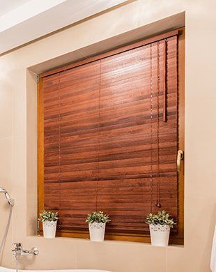 Bathroom window with closed wooden blinds and three small potted plants on the sill