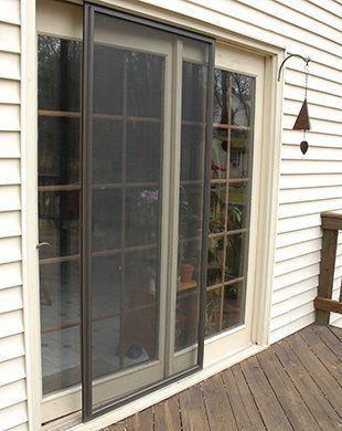 Sliding glass door on a wooden deck beside white siding, with a screen door partly open.