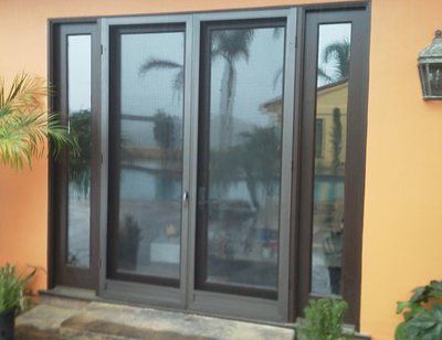 Dark gray glass double doors set in an orange exterior wall with potted plants nearby