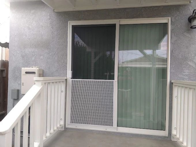 Sliding glass patio door with white railing and railing posts on a gray exterior wall