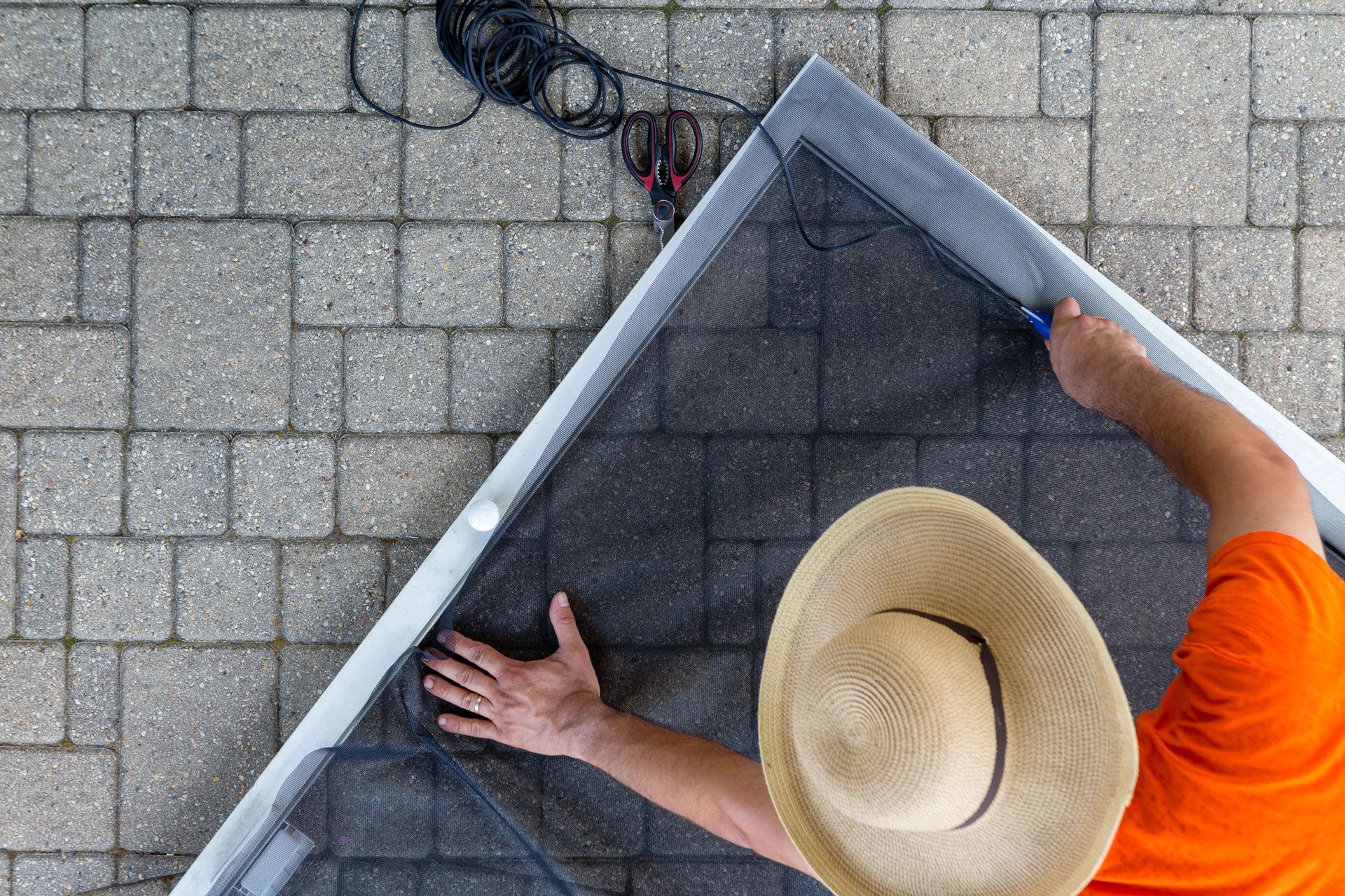 Person in a straw hat and orange shirt installing a dark mesh screen on a roof.