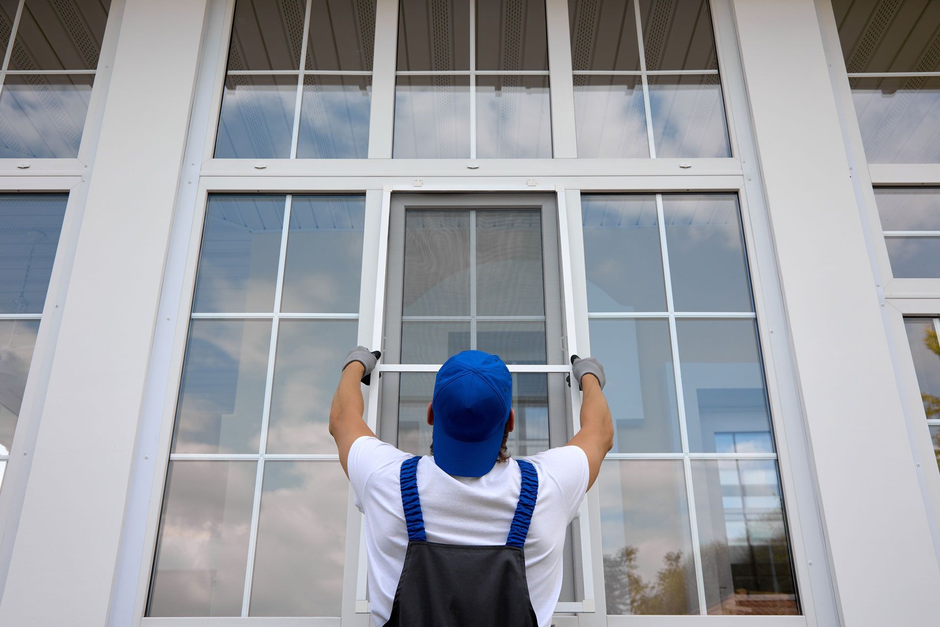 Worker in blue hard hat and overalls cleaning a large window with a squeegee