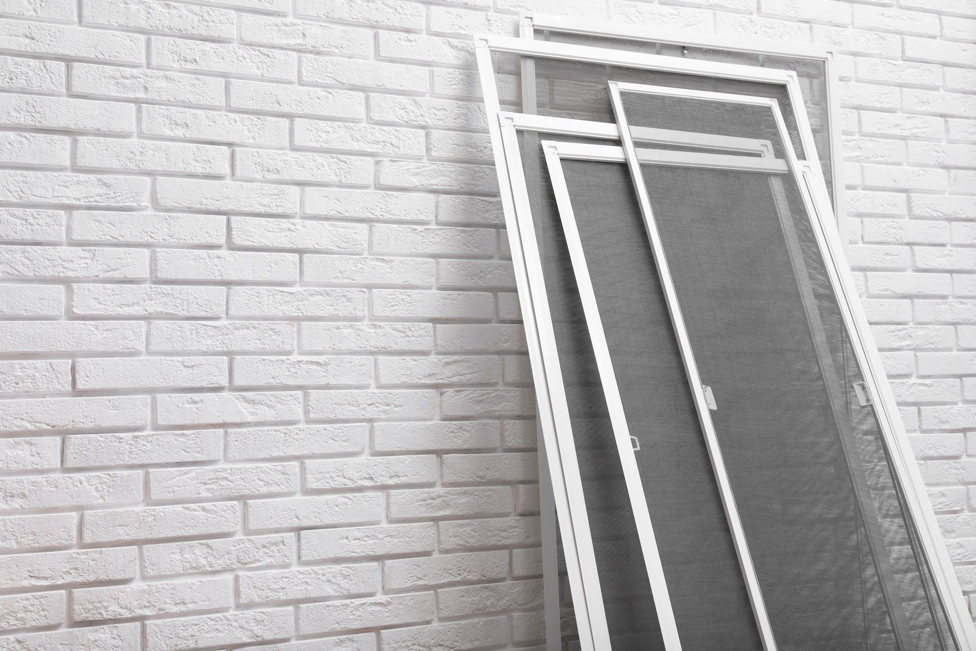 White-framed window screen leaning against a light brick wall