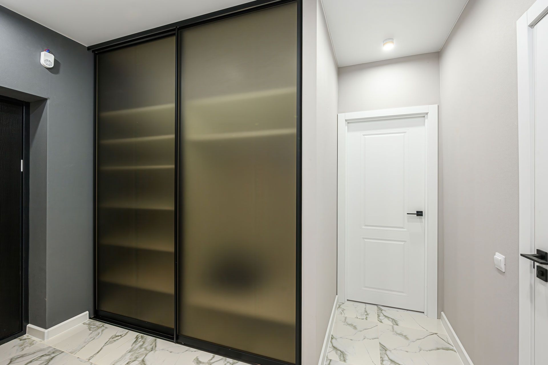 Modern hallway with black-framed frosted wardrobe doors and white interior doors on marble flooring