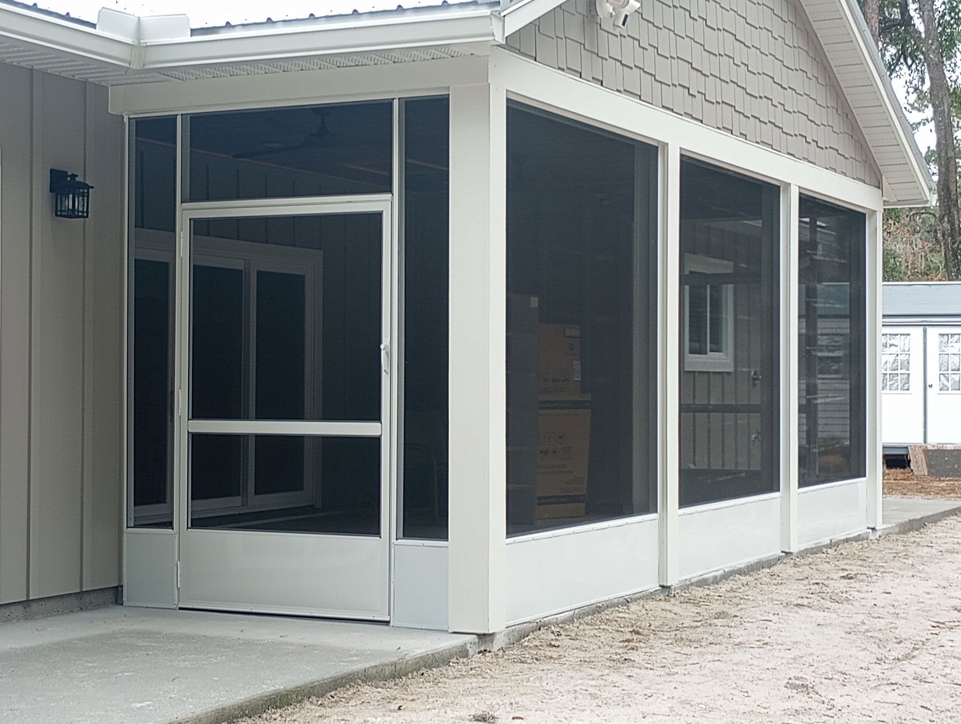 Screened porch on a house with white trim and dark mesh panels beside a gravel path