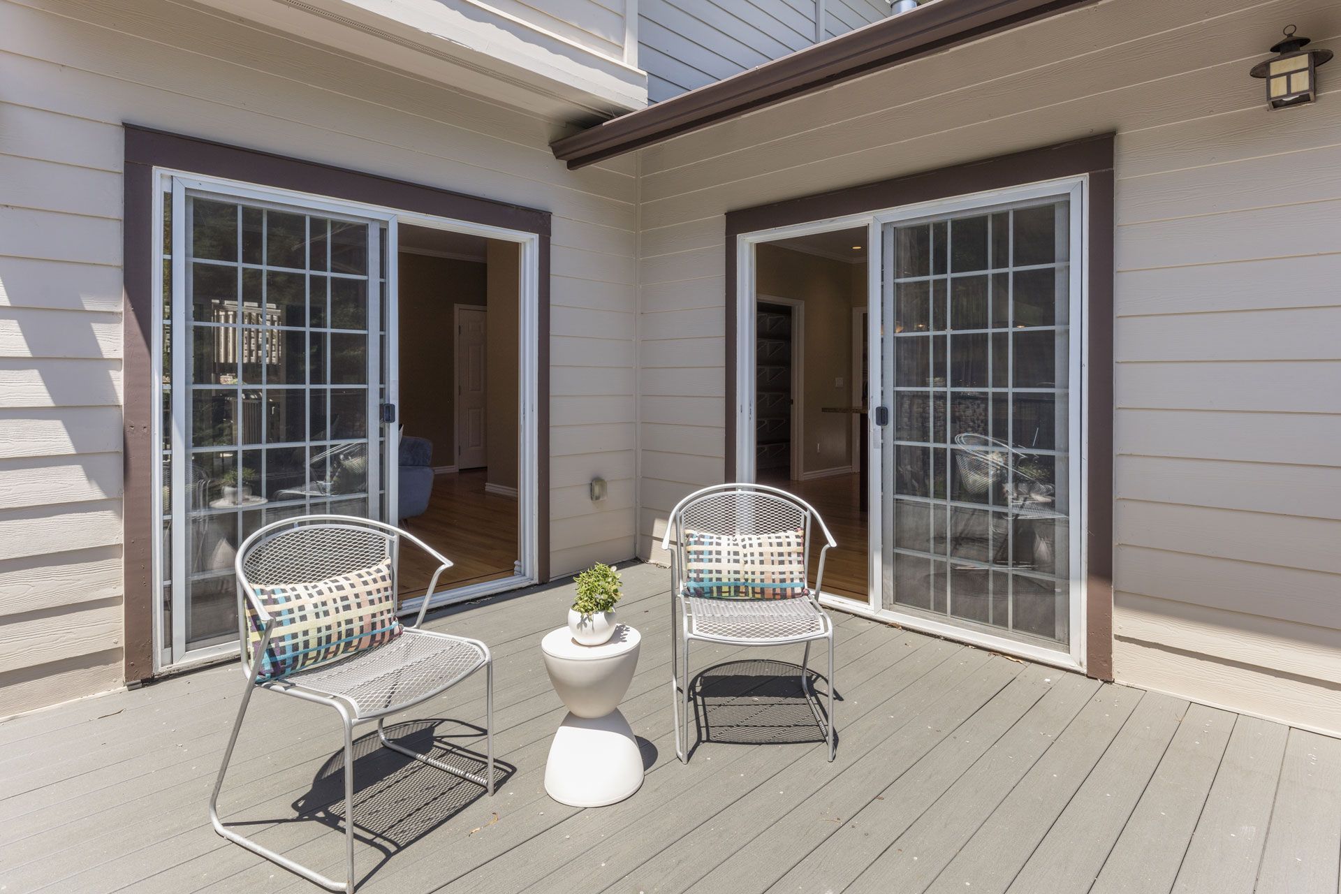 Patio with two white chairs and a small white table in front of sliding glass doors at a house