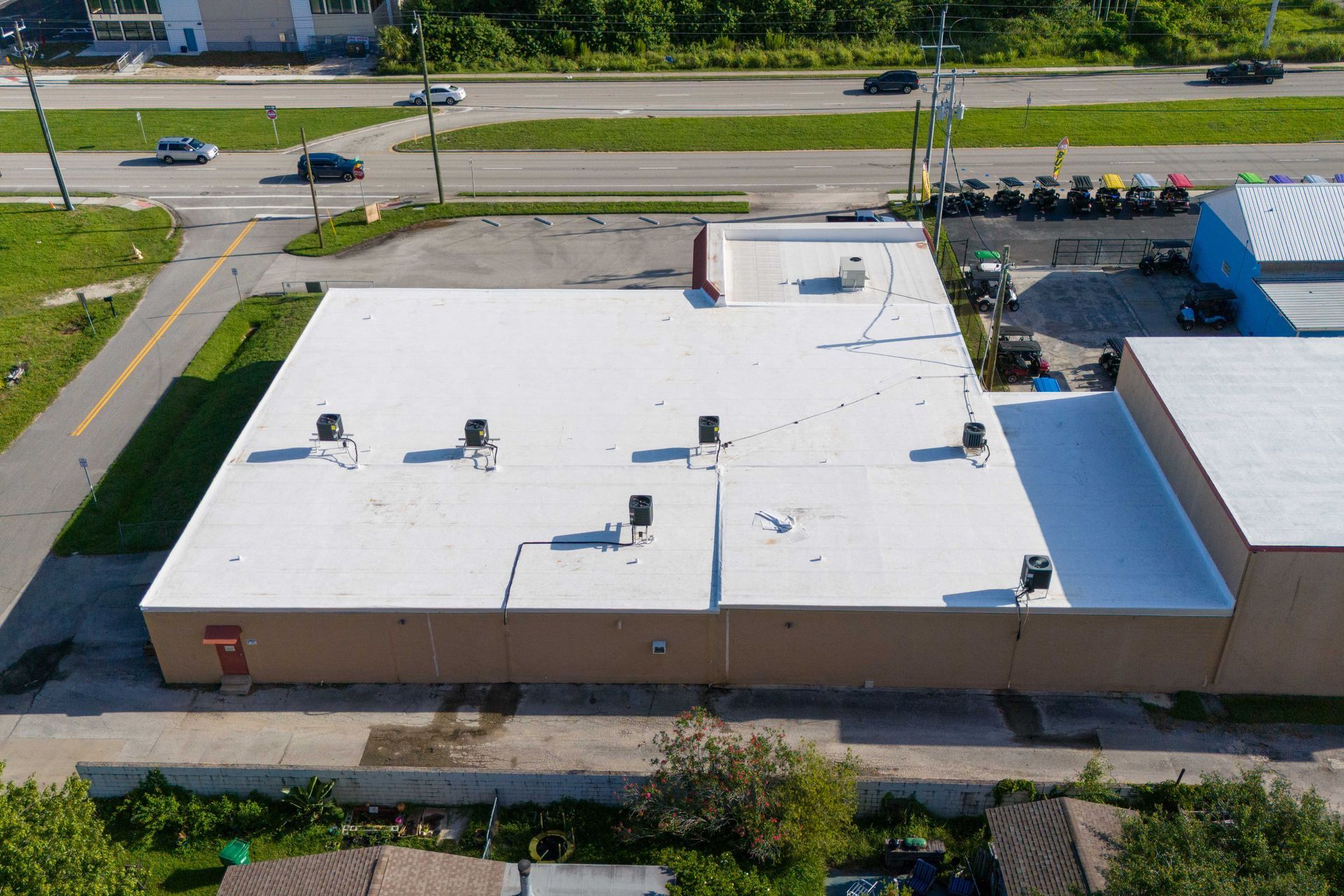 A top-down aerial view of a house roof featuring a mix of grey shingled and flat-roof sections surrounded by green trees.